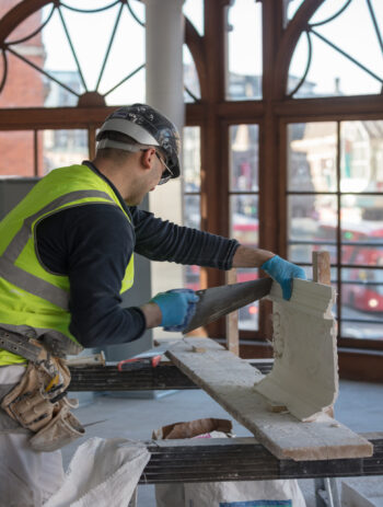 Detailed close-up of an expert artisan restoring original plaster cornices and decorative mouldings on the historic Arding and Hobbs building in central London. Professional heritage conservation and architectural restoration craftsmanship on a landmark London structure.
