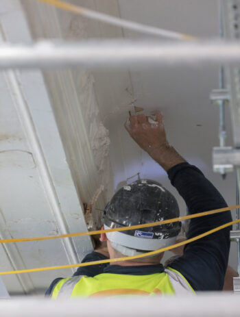 Close-up of a highly skilled professional craftsman expertly repairing historic cornice and intricate plaster mouldings at the iconic Arding and Hobbs building in London. Specialist heritage restoration work preserving traditional architectural details on a Grade II listed building.