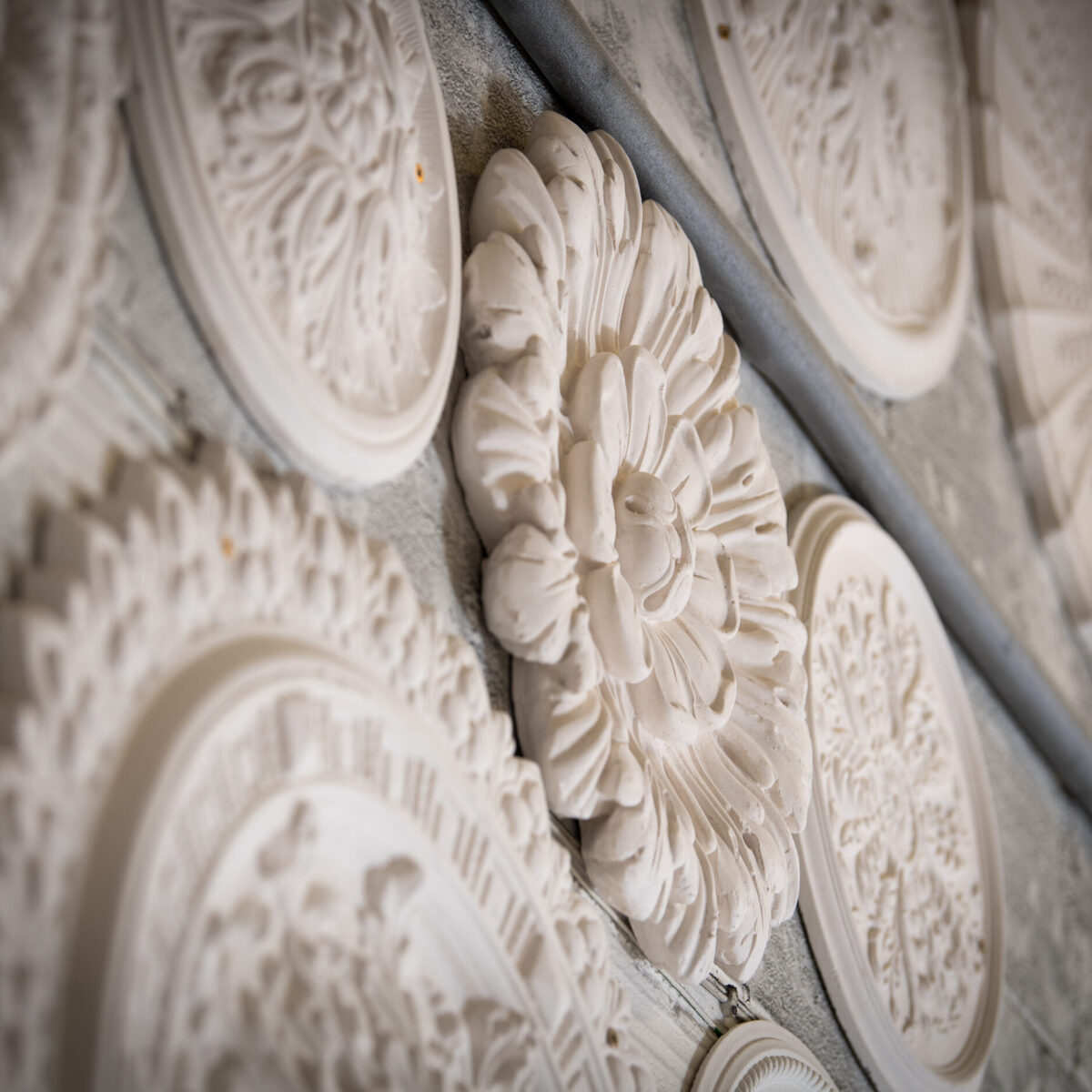 Collection of ornate plaster ceiling roses from historic designs displayed on workshop wall